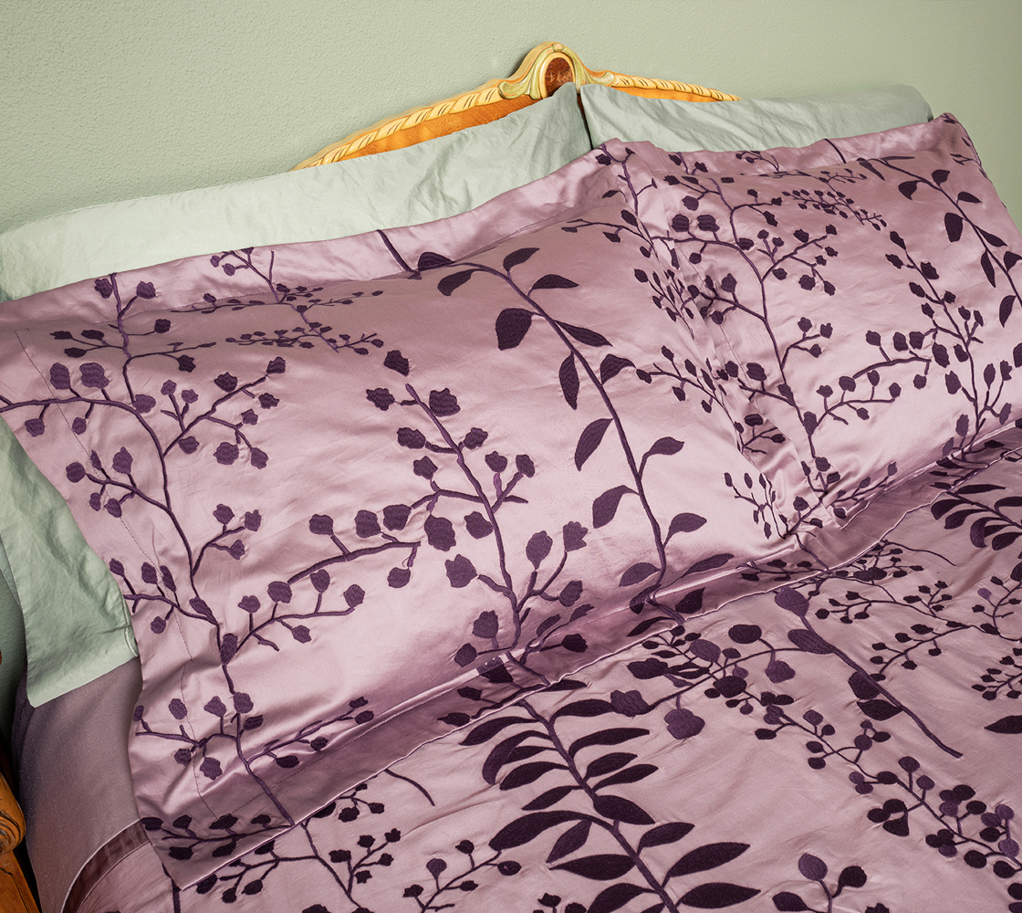 Floral patterned bedding set on a bed with a light green pillow and headboard.